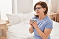Middle age woman drinking cup of coffee sitting on bed at bedroom Royalty Free Stock Photo