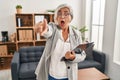 Middle age woman with grey hair at consultation office pointing with finger surprised ahead, open mouth amazed expression, Royalty Free Stock Photo