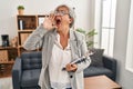 Middle age woman with grey hair at consultation office shouting and screaming loud to side with hand on mouth