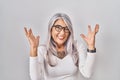 Middle age woman with grey hair standing over white background celebrating mad and crazy for success with arms raised and closed Royalty Free Stock Photo