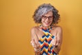 Middle age woman with grey hair standing over yellow background showing middle finger doing fuck you bad expression, provocation Royalty Free Stock Photo