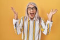 Middle age woman with grey hair standing over yellow background wearing glasses celebrating mad and crazy for success with arms Royalty Free Stock Photo