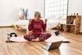 Middle age woman with grey hair training at home looking at exercise video on laptop very happy and excited doing winner gesture Royalty Free Stock Photo