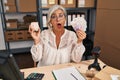 Middle age woman with grey hair working at small business ecommerce holding piggy bank and zloty in shock face, looking skeptical Royalty Free Stock Photo
