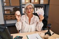 Middle age woman with grey hair working at small business ecommerce holding piggy bank and zloty winking looking at the camera Royalty Free Stock Photo
