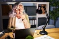 Middle age woman with grey hair working using computer laptop late at night bored yawning tired covering mouth with hand Royalty Free Stock Photo