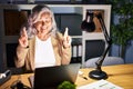 Middle age woman with grey hair working using computer laptop late at night gesturing finger crossed smiling with hope and eyes