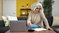 Middle age woman with grey hair writing on notebook accounting at home