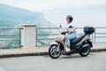 Middle-age woman in helmet and sunglasses on motor scooter on the Sicilian old town streets in the Forza d`Agro with Sant`Alessi