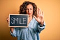 Middle age woman holding blackboard with smile message over isolated yellow background with open hand doing stop sign with serious Royalty Free Stock Photo