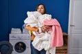 Middle age woman holding dirty laundry ready to put it in the washing machine puffing cheeks with funny face Royalty Free Stock Photo