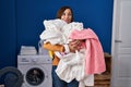 Middle age woman holding dirty laundry ready to put it in the washing machine smiling looking to the side and staring away Royalty Free Stock Photo