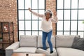 Middle age woman listening to music and dancing standing on sofa at home Royalty Free Stock Photo