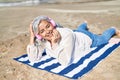 Middle age woman listening to music lying on towel at seaside Royalty Free Stock Photo