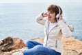 Middle age woman listening to music sitting on the rock at seaside Royalty Free Stock Photo