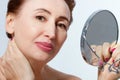 Middle age woman with mirror, touching her neck. Macro female face. Menopause. Anti-aging collagen