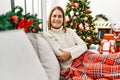 Middle age woman sitting on the sofa by christmas tree happy face smiling with crossed arms looking at the camera Royalty Free Stock Photo