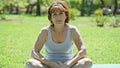 Middle age woman sitting on yoga mat with serious face at park Royalty Free Stock Photo