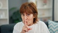 Middle age woman smiling confident sitting on sofa doing silent gesture home