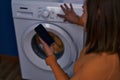 Middle age woman turning on washing machine using smartphone at laundry room Royalty Free Stock Photo