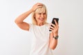 Middle age woman using smartphone standing over isolated white background stressed with hand on head, shocked with shame and Royalty Free Stock Photo