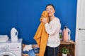 Middle age woman washing clothes touching softener sweater with face at laundry room