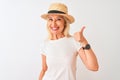 Middle age woman wearing casual t-shirt and hat standing over isolated white background doing happy thumbs up gesture with hand