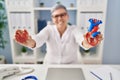 Middle age woman wearing doctor uniform holding heart ventricles at clinic