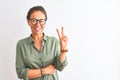 Middle age woman wearing green shirt and glasses standing over isolated white background smiling with happy face winking at the Royalty Free Stock Photo