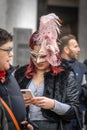 A middle-age woman wearing mask with the feathers stands looking in her smartphone at carnival in Venice, Italy Royalty Free Stock Photo