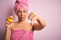 Middle age woman wearing pink bath towel from beauty body care holding rubber yellow duck with angry face, negative sign showing