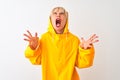 Middle age woman wearing rain coat with hood standing over isolated white background crazy and mad shouting and yelling with