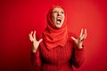Middle age woman wearing traditional muslim hijab standing over isolated red background crazy and mad shouting and yelling with Royalty Free Stock Photo