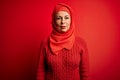 Middle age woman wearing traditional muslim hijab standing over isolated red background with serious expression on face Royalty Free Stock Photo