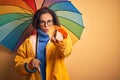 Middle age woman wearing yellow raincoat under colorful umbrella over isolated background pointing with finger to the camera and Royalty Free Stock Photo