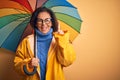 Middle age woman wearing yellow raincoat under colorful umbrella over isolated background surprised with an idea or question Royalty Free Stock Photo