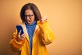 Middle age woman wearing yellow raincoat using smartphone over isolated yellow background annoyed and frustrated shouting with Royalty Free Stock Photo