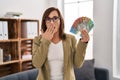 Middle age woman working at consultation office holding australian dollars covering mouth with hand, shocked and afraid for Royalty Free Stock Photo