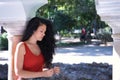 Middle-aged adult Hispanic woman with black curly hair, leaning on a column, thoughtfully touching her hair. Concept thoughts,