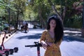 Middle-aged adult Hispanic woman with black curly hair, wearing a colorful outfit, leaning on an electric scooter. Concept scooter Royalty Free Stock Photo