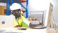 Middle aged African American warehouse worker working on personal computer and preparing a shipment in large warehouse Royalty Free Stock Photo