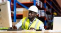 Middle aged African American warehouse worker working on personal computer and preparing a shipment in large warehouse Royalty Free Stock Photo