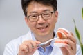 A middle-aged Asian dentist holding dental models and toothbrushes in his hand