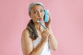 Middle aged Asian lady with bath towel holds toothbrush using sponge as phone in studio