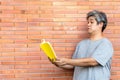 Middle-aged Asian man has gray hair, is reading a book By holding it away from the eyes, because he has farsightedness