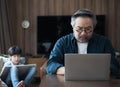 Middle-aged Asian man using laptop work from home with son draws a picture on the back. Royalty Free Stock Photo