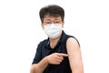 A middle-aged Asian man wearing a medical mask pointing to an arm injected with a vaccine.