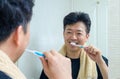 A middle-aged Asian man who wears a towel around his neck and brushing teeth in the bathroom Royalty Free Stock Photo