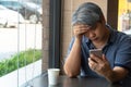 Middle-aged Asian men 40 years old, stressed and tired and using smartphone, are sitting in fast restaurant. On the table there