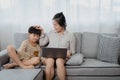 A middle-aged Asian single mom is working on a laptop on the sofa in the living room of the house. The son ran and jumped onto the Royalty Free Stock Photo